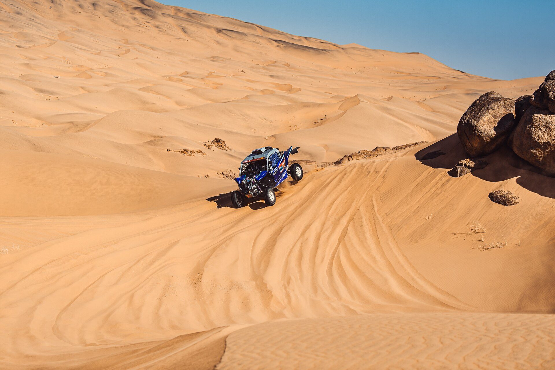 Small SSV driving through a vast sea of sand dunes during the Dakar Rally
