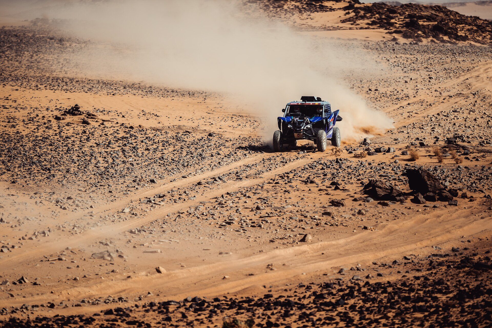 Distant SSV raising a dust trail on a sand and stone track in the desert